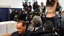 Mantan PM Italia dan pemimpin partai Forza Italia Silvio Berlusconi meninggalkan seorang wanita yang melakukan aksi topless saat pemungutan suara di Milan, Italia, Minggu (4/3). Aksi itu dilakukan di sebuah TPS. (Daniel Dal Zennaro/ANSA via AP)