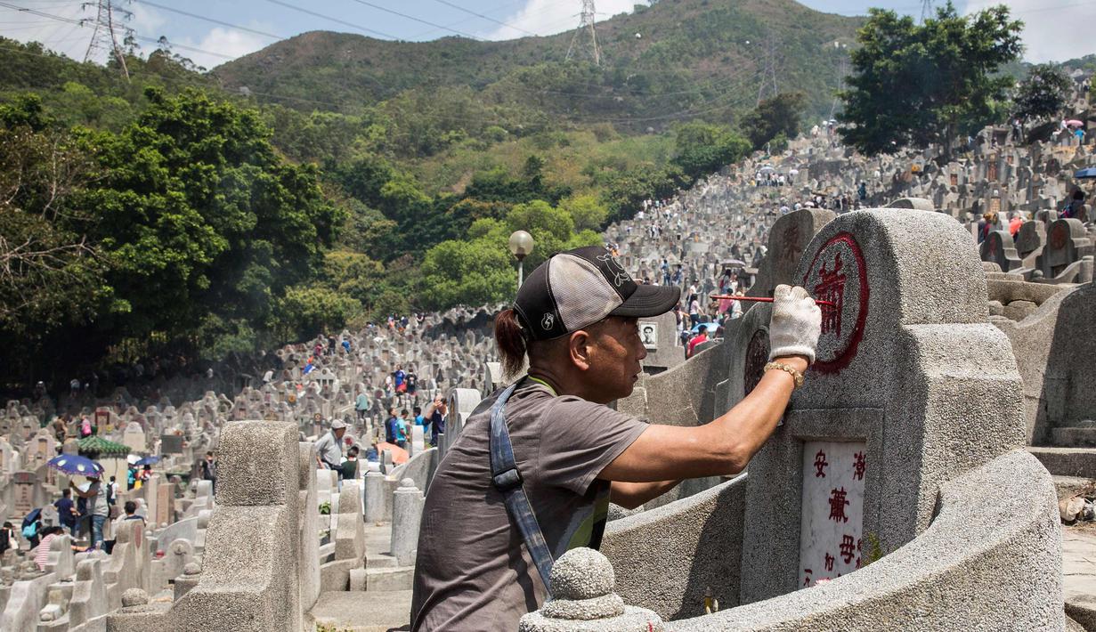 Seorang pria melukis ulang nama yang pudar di makam kerabat selama festival Qingming di pemakaman di Hong Kong (5/4). Biasanya warga cenderung membuat persembahan untuk keluarga atau kerabat mereka agar tetap nyaman di akhirat. (AFP Photo/Isaac Lawrence)