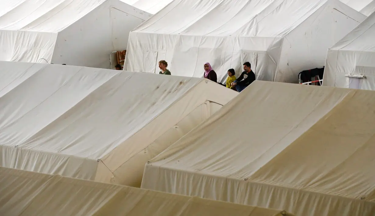 Orang berkumpul di dekat tenda yang didirikan bagi para migran di dalam hanggar bekas bandara Tempelhof di Berlin, Jerman, Rabu (9/12/2015). Jerman menerima satu juta migran dari beberapa negara yang sedang dilanda perang. (REUTERS/Fabrizio Bensch)