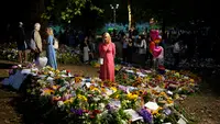 Seorang wanita membaca pesan yang ditempatkan di antara karangan bunga untuk Ratu Elizabeth II di Green Park, dekat Istana Buckingham di London, Senin (12/9/2022). Sebelum menjabat Ratu Inggris, Elizabeth menerima pendidikan di rumah melalui guru pribadinya yang bernama Henry Marten. (AP Photo/Markus Schreiber)