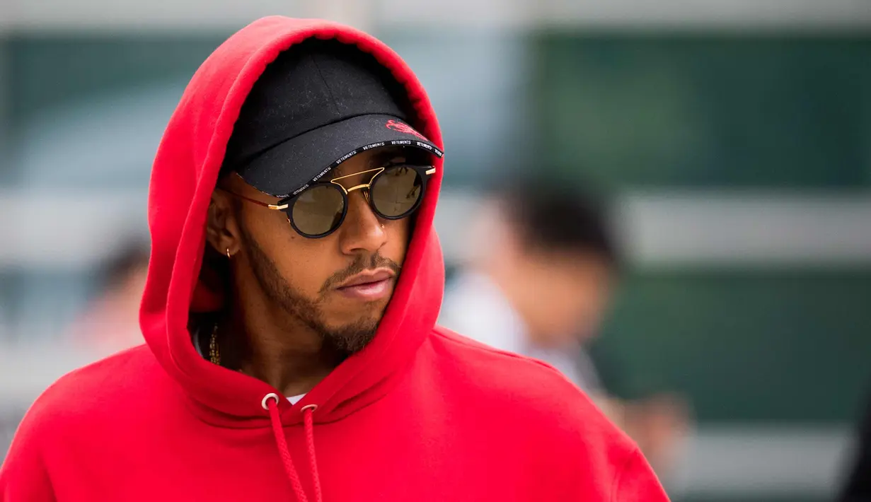 Pembalap Mercedes asal Inggris Lewis Hamilton berjalan di paddock sebelum Grand Prix Formula Satu China di Shanghai (12/4). Hamilton keren mengenakan kaca mata dan jaket berwarna merah. (AFP Photo/Johannes Eisele)