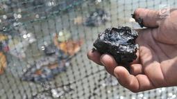 Nelayan menunjukkan oil spill yang telah membeku di sekitar tambak penangkap udang di perairan Muara Beting, Muara Gembong, Bekasi, Jawa Barat, Minggu (28/7/2019). Oil spill tersebut merupakan milik Pertamina Hulu Energi di blok migas ONWJ. (merdeka.com/Iqbal S. Nugroho)