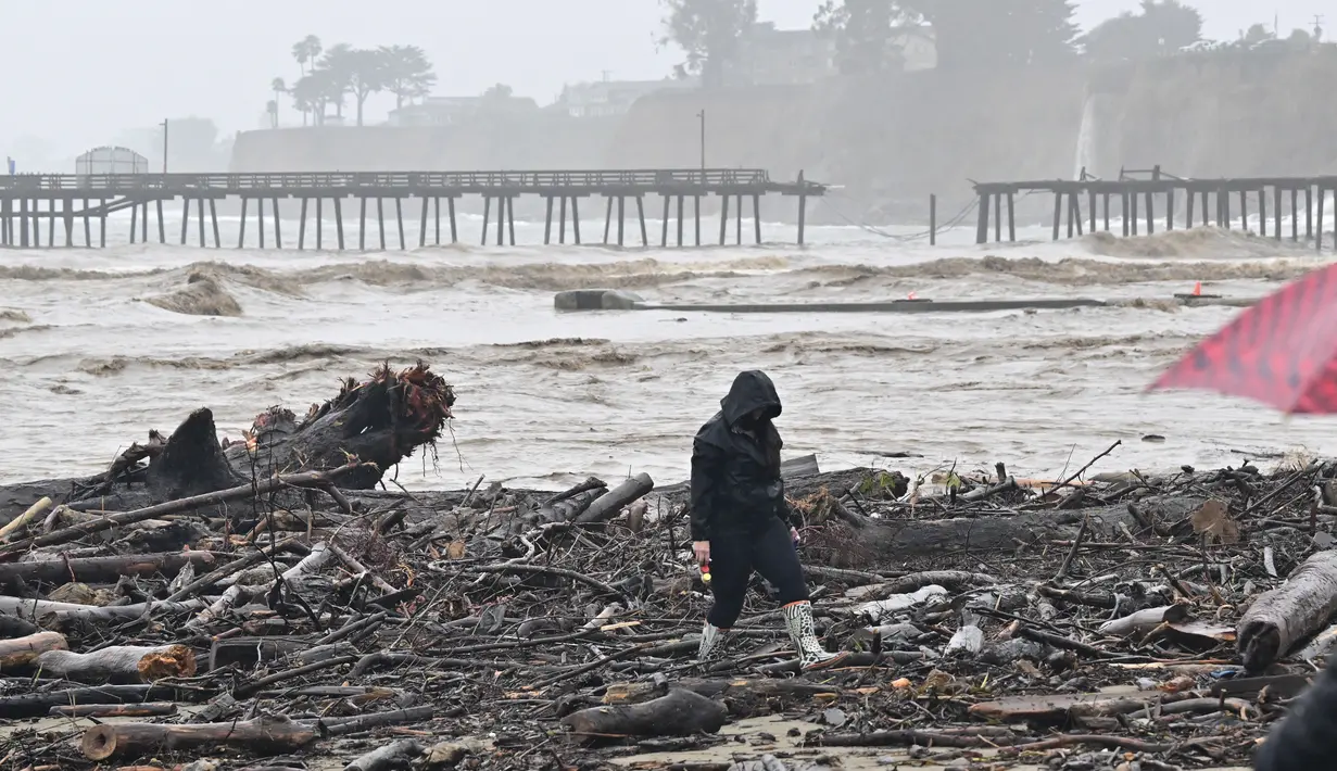 Warga berjalan di dekat Dermaga Capitola yang terbelah dua dari Aptos, California pada 9 Januari 2023. Badai besar yang disebut "badai bom" oleh ahli meteorologi telah tiba dan diperkirakan akan menyebabkan banjir yang meluas di seluruh negara bagian. (AFP/Josh Edelson)