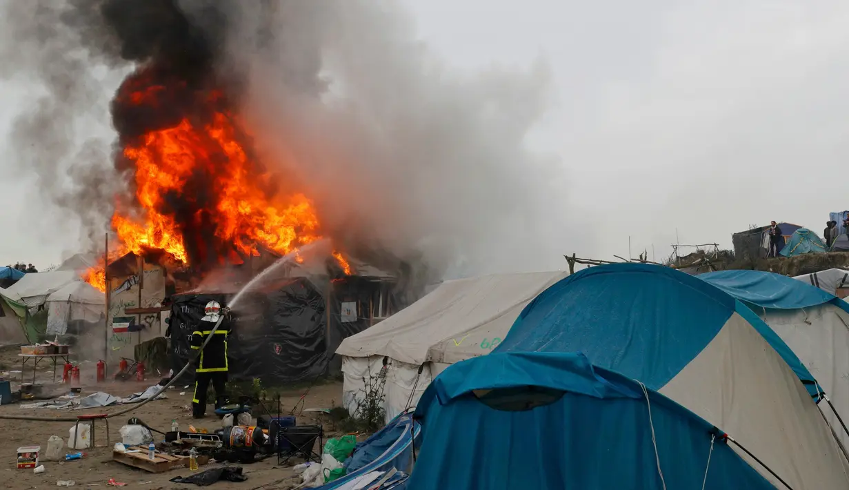 Petugas memadamkan kobaran api di pengungsian imigran "Jungle", di kota pelabuhan Calais, Prancis (26/10). Karena kumuh pemerintah Prancis akhirnya mulai mengosongkan kamp pengungsian imigran tersebut. (REUTERS/Philippe Wojazer)