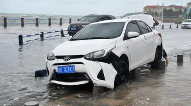 Sebuah mobil rusak setelah dihantam ombak yang disebabkan Topan Yagi di sepanjang pantai laut di Qingdao di provinsi Shandong timur China (13/8). Lebih dari 200.000 warga mengungsi saat topan mencapai daratan pantai timur. (AFP Photo)