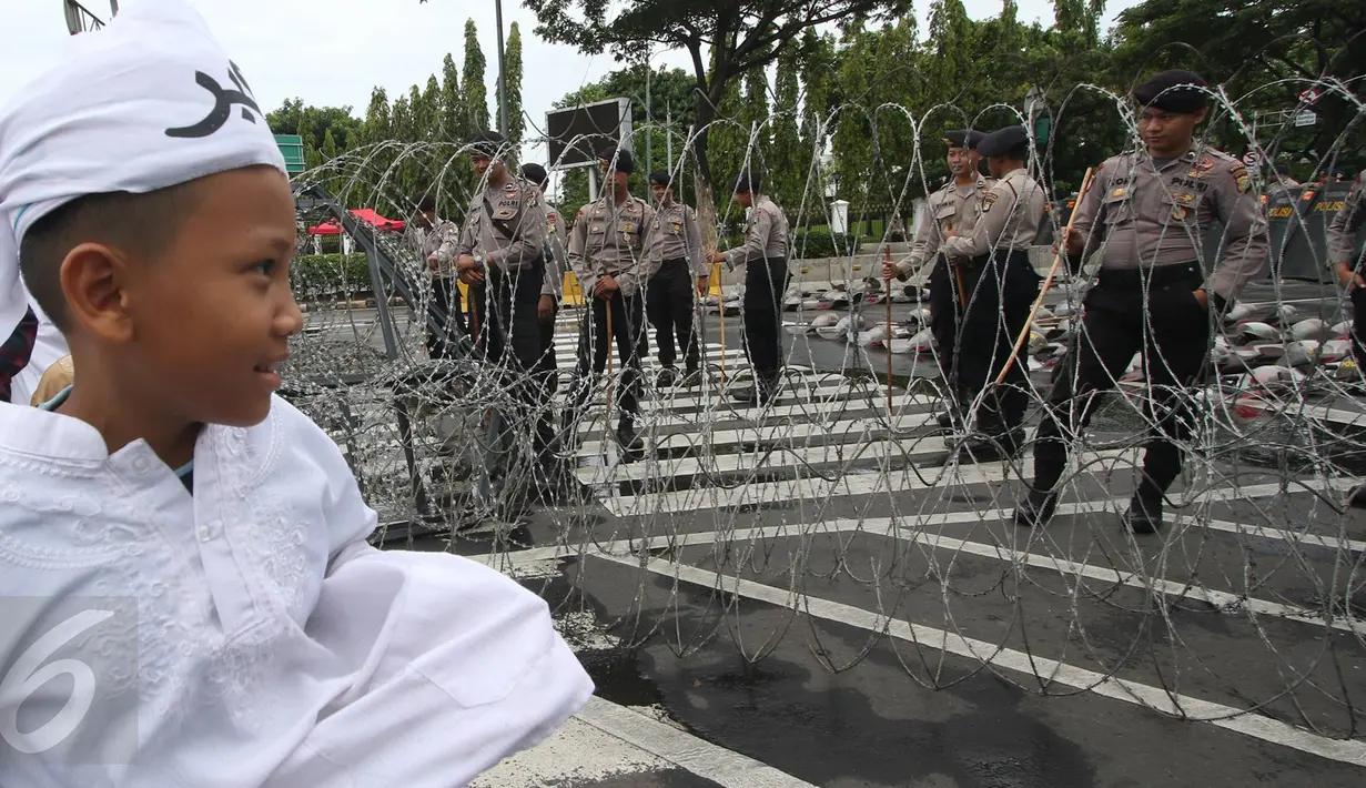 Seorang anak melintasi petugas polisi yang sedang memasang kawat berduri di sekitar Istana Negara, Jakarta, Jumat (31/3). Kawat berduri tersebut dipasang untuk mengantisipasi ricuh aksi 31 Maret. (Liputan6.com/Immanuel Antonius)
