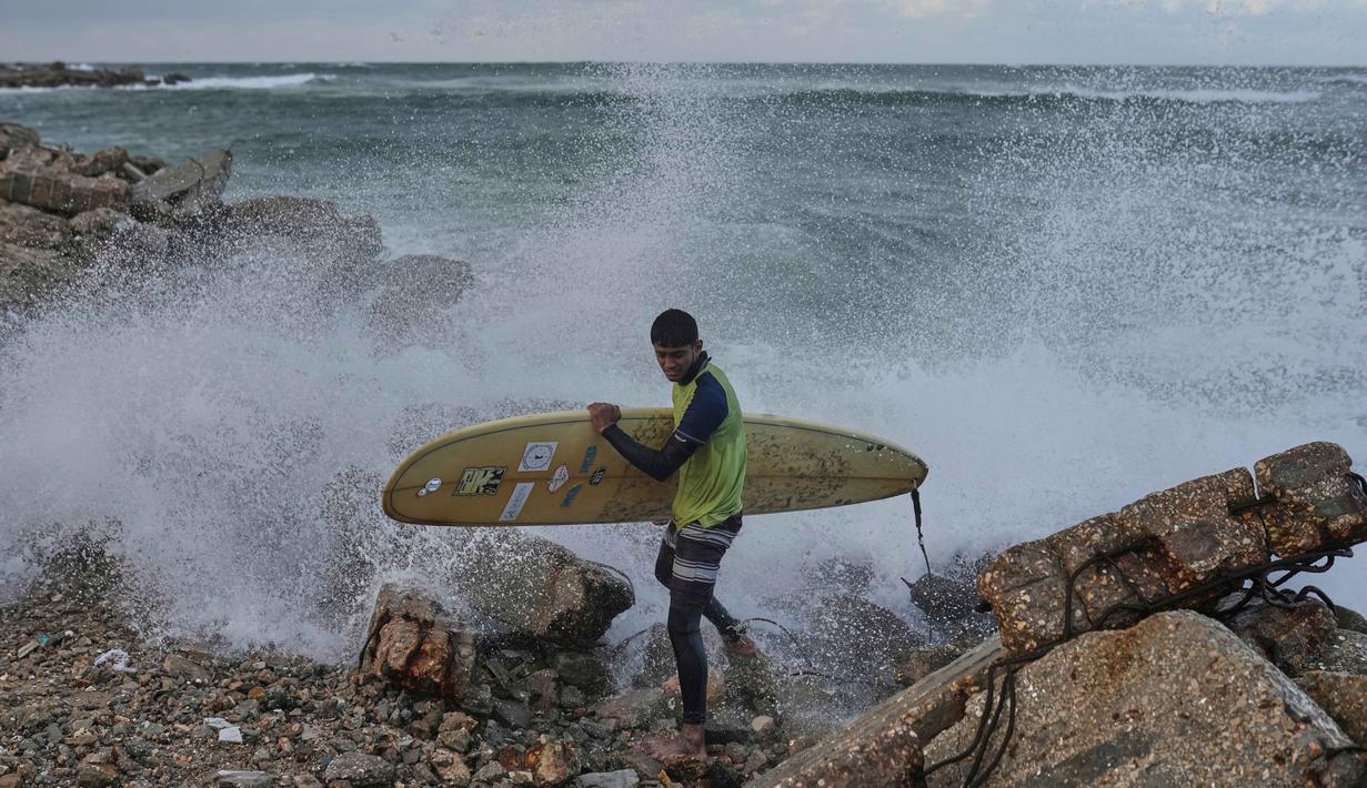 Seperti yang dilakukan peselancar lokal seperti Khalil Abu Jayyab dan Tahseen Abu Assi yang terpantau masih turun ke laut untuk menunggangi ombak di sepanjang garis pantai Kota Gaza yang rusak pada Minggu, 28 Desember 2025. Tampak dalam foto, warga Palestina, Khalil Abu Jayyab membawa papan selancarnya saat memasuki sepanjang garis pantai di Kota Gaza, Minggu, 28 Desember 2025. (AP Photo/Jehad Alshrafi)