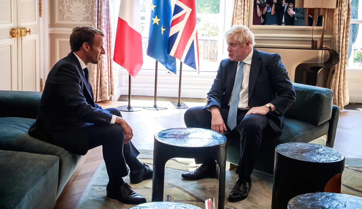 Presiden Prancis Emmanuel Macron berbincang dengan PM Inggris, Boris Johnson dalam kunjungan kenegaraan di Istana Elysee, Paris, Kamis (22/8/2019). Dalam pertemuan, Johnson tertangkap kamera bercanda ke arah kamera dan meletakkan kakinya di meja kopi. (Christophe Petit Tesson, Pool via AP)