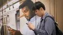 Penumpang kereta bermain handphone dengan latar belakang iklan larangan hoax di Stasiun Kereta Kuala Lumpur, Malaysia, Senin (2/4). Pengesahan UU Antihoax dikhawatirkan membungkam kelompok yang berseberangan dengan pemerintah. (AP Photo/Vincent Thian)