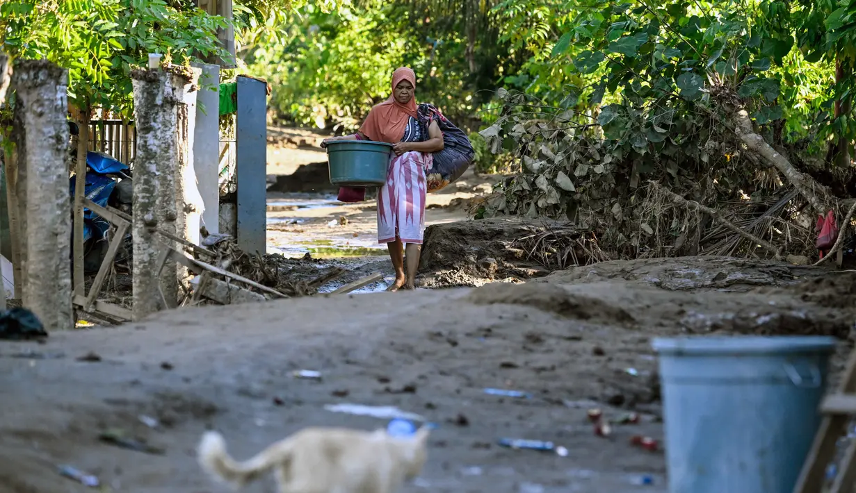 Ratusan rumah terendam, puluhan rusak berat, ribuan warga mengungsi, dan akses jalan utama masih terputus di sejumlah titik. Tampak dalam foto, seorang warga membawa barang-barangnya di jalan yang tertutup lumpur setelah banjir bandang di Meureudu, Kabupaten Pidie Jaya, Provinsi Aceh, pada 29 November 2025. (CHAIDEER MAHYUDDIN/AFP)