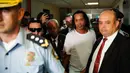 Mantan pemain timnas Brasil, Ronaldinho dikawal oleh polisi meninggalkan kantor pengadilan di Asuncion, ibu kota Paraguay, Jumat (6/3/2020). Ronaldinho bersama saudara laki-lakinya berurusan dengan pihak berwenang Paraguay karena menggunakan paspor palsu untuk memasuki negara itu. (AP/Jorge Saenz)