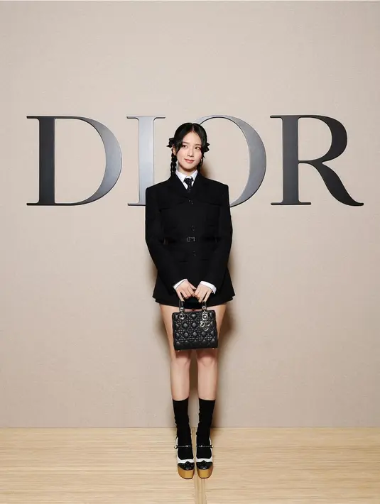 Jisoo BLACKPINK sukses gebrak PFW dengan tampilan ala Wednesday Addams. Ia mengenakan jaket dan short silk dan wool di atas kemeja putih. Ia jinjing Lady Dior, kenakan heels dan kaus kaki panjang [Dior]