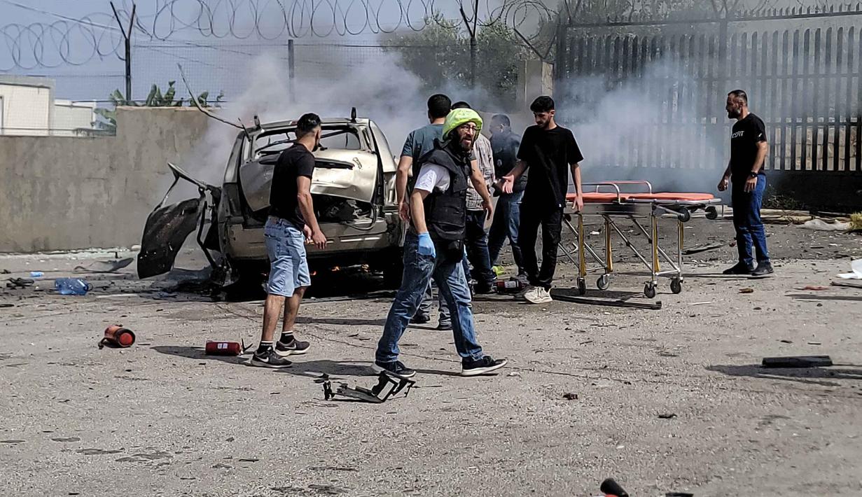 Petugas pertolongan pertama dan warga yang lewat berkumpul di sekitar reruntuhan kendaraan yang menjadi sasaran serangan pesawat tak berawak Israel di kota Jiyeh, Selatan Beirut, pada Rabu 13 Mei 2026. (Fadel ITANI/AFP)