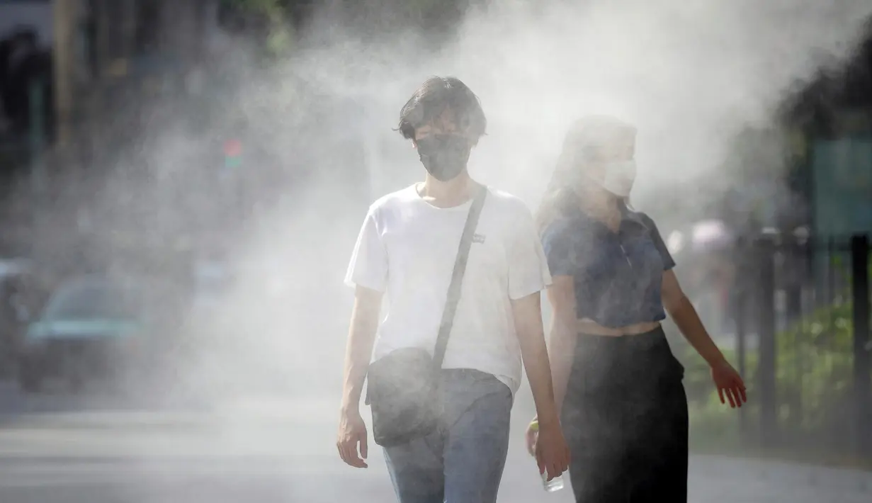 Orang-orang yang memakai masker wajah untuk membantu melindungi diri dari penyebaran virus corona melakukan pendinginan di titik kabut yang menyejukkan, Tokyo, Jepang, 1 Agustus 2022. Cuaca panas terus berlanjut di wilayah metropolitan karena suhu diperkirakan akan meningkat hingga 35 derajat Celcius (95 derajat Fahrenheit), menurut biro meteorologi Jepang. (AP Photo/Eugene Hoshiko)