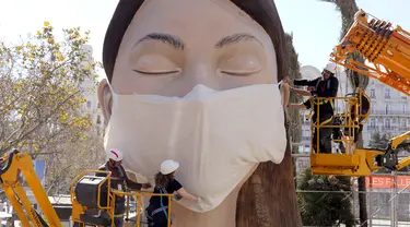 Pekerja memasang masker di salah satu patung raksasa yang akan ditampilkan di festival Las Fallas atau festival api di Valencia, Spanyol, Rabu (11/3/2020). Festival Fallas yang akan berlangsung pada 13 Maret telah dibatalkan karena wabah coronavirus. (AP Photo/Alberto Saiz)