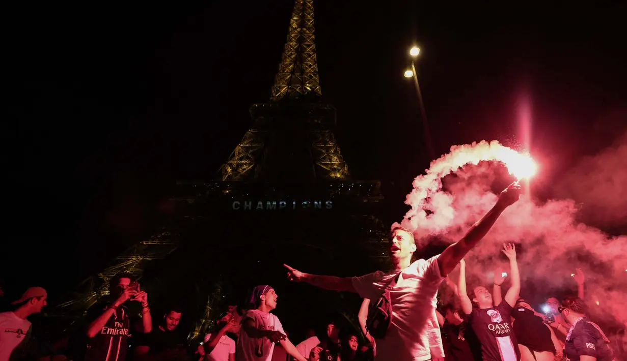 Para pendukung Paris Saint-Germain (PSG) menyalakan suar di depan Menara Eiffel, Paris, Prancis pada 31 Mei 2025 waktu setempat atau Minggu 1 Juni 2025 dini hari WIB. (Thibaud MORITZ/AFP)