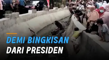 Seorang pria mengenakan kaos warna hitam dan anak kecil mengambil bingkisan dari Presiden Joko Widodo yang jatuh di selokan.