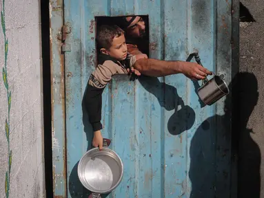 Warga Palestina yang terlantar, anak-anak, dan dewasa, menunggu makanan di sebuah tempat penampungan yang telah dihuni keluarga-keluarga di Nuseirat, pusat Jalur Gaza, pada 23 November 2025. Badan kemanusiaan Perserikatan Bangsa Bangsa (PBB) untuk Koordinasi Urusan Kemanusiaan (OCHA) mengatakan pada Sabtu 22 November 2025 bahwa peningkatan bantuan untuk Gaza masih terhambat. (EYAD BABA/AFP)