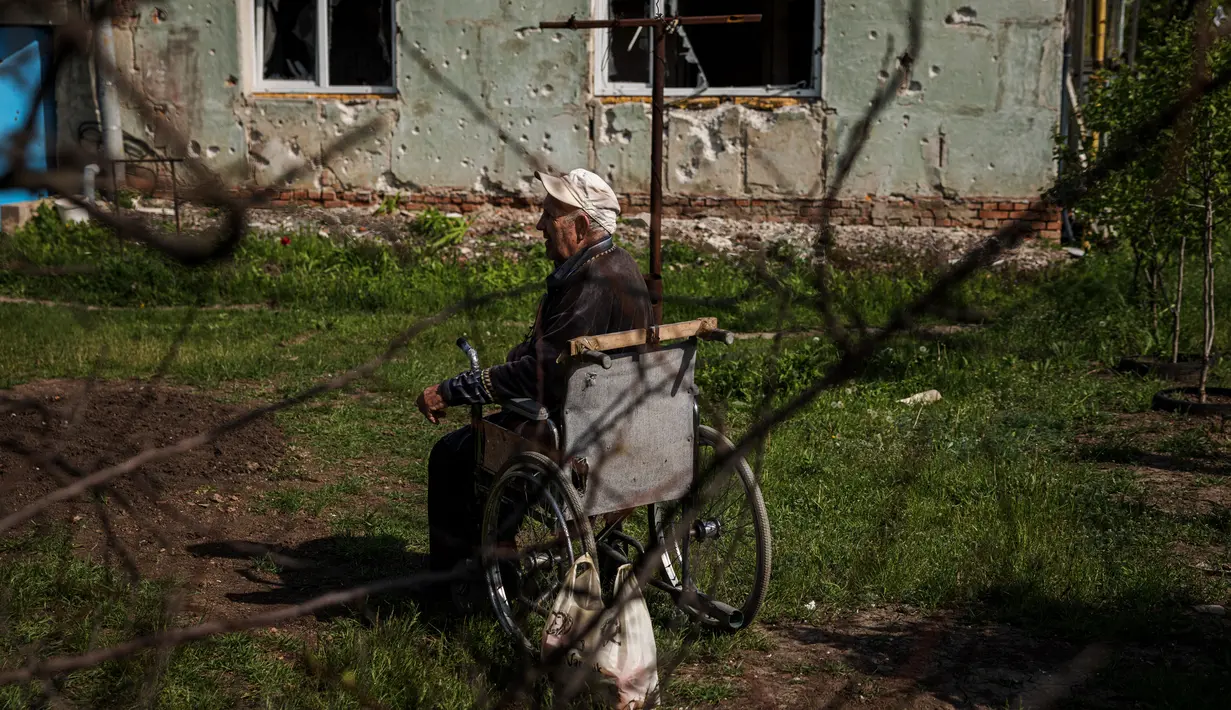 <p>Seorang pria lanjut usia duduk di kursi roda setelah menerima bantuan kemanusiaan, di tengah invasi Rusia ke Ukraina, di desa Vilkhivka, dekat kota timur Kharkiv, pada 14 Mei 2022. Puluhan rumah di Vilkhivka, sebuah desa berpenduduk sekitar 2.000 jiwa, hancur oleh peluru, ledakan atau kebakaran. Puing-puing berserakan di jalan-jalan termasuk selongsong peluru, dan sisa-sisa amunisi. (Dimitar DILKOFF / AFP)</p>