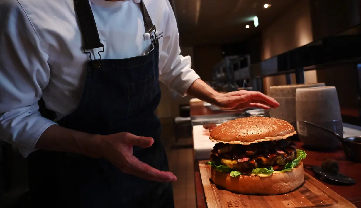 Chef dari restoran The Oak Door, Patrick Shimada berpose dengan burger raksasa di hotel Grand Hyatt Tokyo, Senin (1/4). Hamburger ini memiliki diameter 25 centimeter dan berisi foie gras, daging sapi Jepang, dan jamur truffle hitam segar. (CHARLY TRIBALLEAU/AFP)