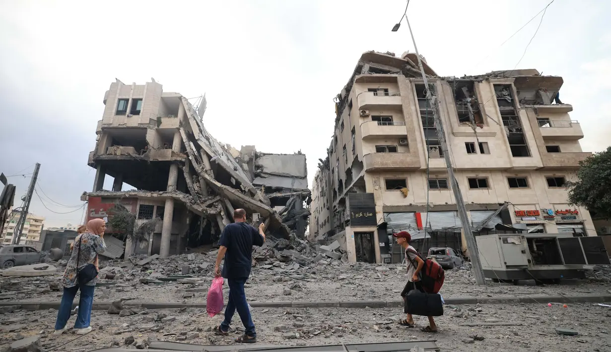 Warga Palestina membawa barang-barang pribadi berjalan melewati bangunan yang rusak parah setelah serangan udara Israel di distrik al-Rimal, Kota Gaza, pada 10 Oktober 2023. (Mahmud HAMS/AFP)