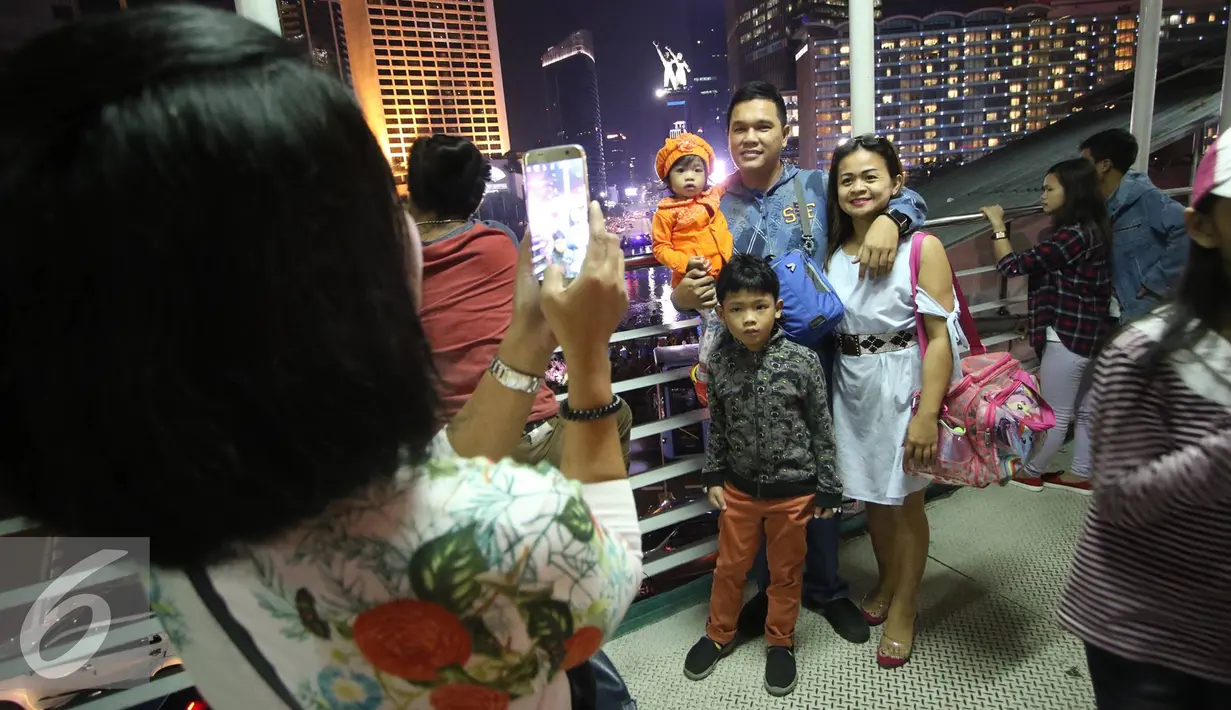 Sejumlah warga berfoto bersama di jembatan penyebrangan kawasan Bundaran HI di Jakarta, Sabtu (31/12). Walaupun car free night dibatalkan kawasan tersebut mulai dipadati warga dari berbagai daerah. (Liputan6.com/Immanuel Antonius)