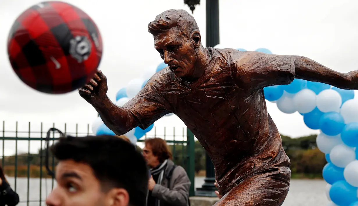 Seorang anak bermain bola di depan patung perunggu Lionel Messi yang baru diresmikan di pusat kota Buenos Aires, Argentina, Selasa (28/6). Patung tersebut guna membujuk Messi membatalkan keputusan pensiun yang sudah diambilnya. (REUTERS/Marcos Brindicci)