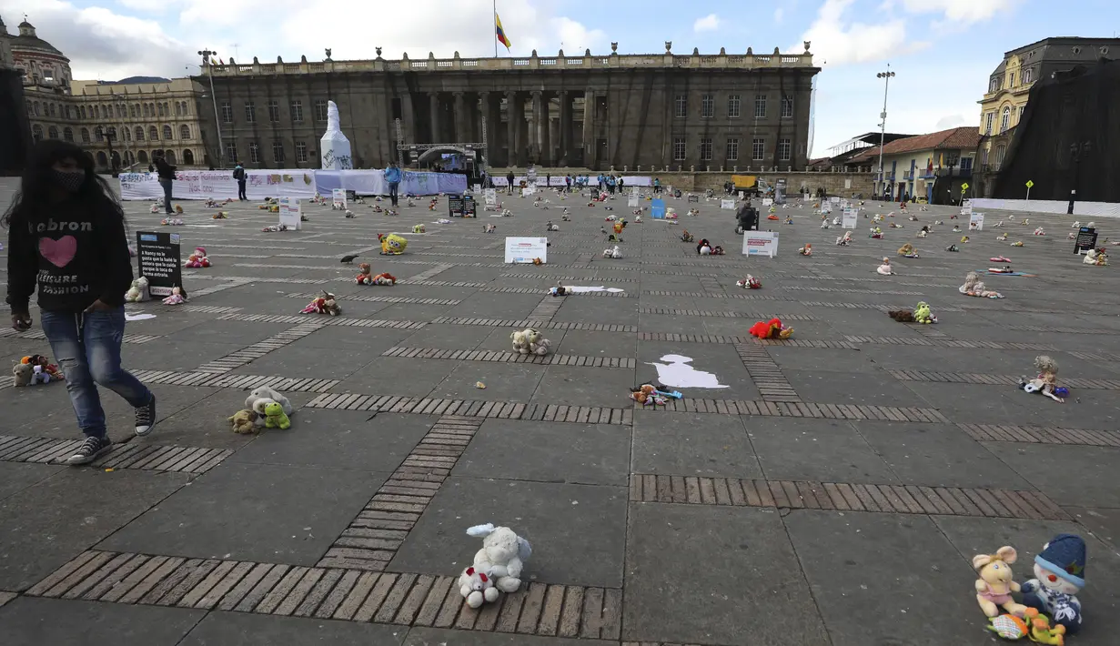 Seorang perempuan melewati mainan yang mewakili anak korban kekerasan selama protes di alun-alun Bolivar di Bogota, Kolombia, Senin (30/11/2020). Ratusan mainan, boneka, dan action figure diletakkan di Bolivar Square untuk memprotes kekerasan terhadap anak-anak. (AP Photo/Fernando Vergara)