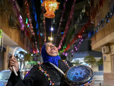 Dalal, seorang wanita Mesir yang dikenal sebagai 'musaharati', berjalan di sepanjang jalan sambil memukul gendang dan menyerukan umat Muslim untuk bangun dan makan sahur selama bulan suci Ramadan di distrik Hadayek el-Maadi, selatan Kairo pada Minggu 1 Maret 2026. Musaharati merupakan tradisi kuno Ramadan di negara-negara Arab, Palestina, Mesir, dan lainnya. (Khaled DESOUKI/AFP)