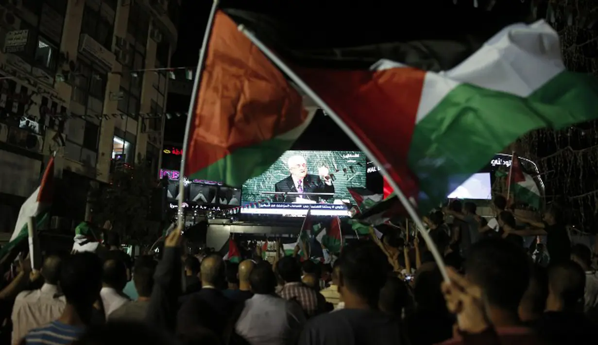 Warga Palestina mengibarkan bendera mereka saat menonton pidato Presiden Palestina, Mahmud Abbas di layar raksasa, Rabu (30/9). Sidang majelis Umum PBB menyetujui untuk mengibarkan bendera Palestina dan Vatikan. (AFP PHOTO/ ABBAS Momani)