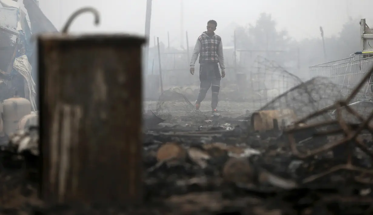 Seorang imigran berada di dekat puing-puing yang hangus terbakar di pengungsian imigran "Jungle", di kota pelabuhan Calais, Prancis (26/10). Setidaknya hingga 8.000 imigran telah dipindahkan ke ratusan tempat pengungsian sementara. (REUTERS/Neil Balai)