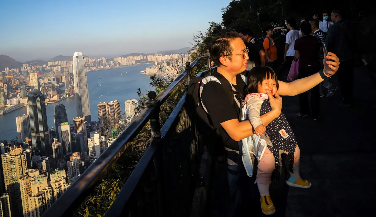 Seorang pria berswafoto dengan bayinya di sepanjang jalur pendakian di Hong Kong pada 22 Februari 2020. Warga Hong Kong memilih pergi ke daerah gunung dan jalur hiking dibandingkan harus tinggal di pusat kota yang sempit dan dibayangi ketakutan akan wabah virus corona (Covid-19). (VIVEK PRAKASH/AFP)