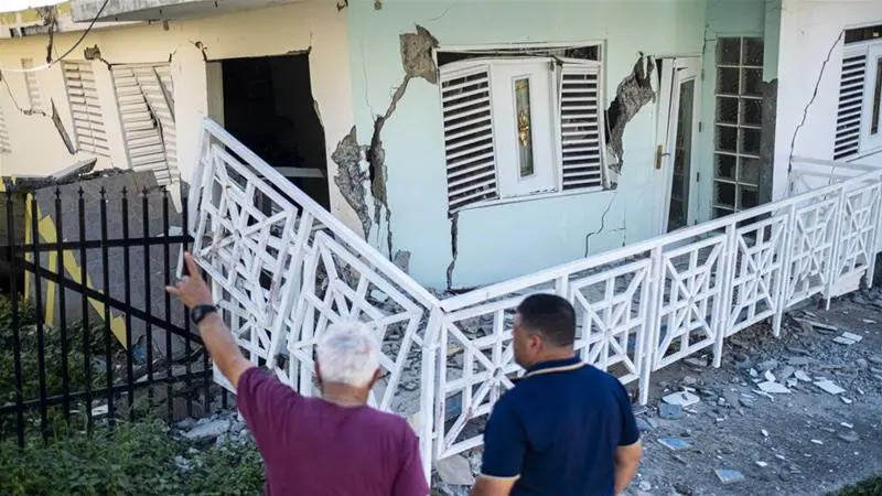 Orang-orang melewati sebuah rumah yang rusak oleh gempa bumi di Guanica, Puerto Rico.