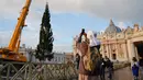 Biarawati mengambil foto saat sebuah derek dikerahkan untuk mendirikan pohon Natal raksasa di Lapangan Santo Petrus, Vatikan, Kamis (22/11). Pohon cemara yang didatangkan dari Hutan Consiglio di Italia ini tingginya mencapai 23 meter (AP/Andrew Medichini)
