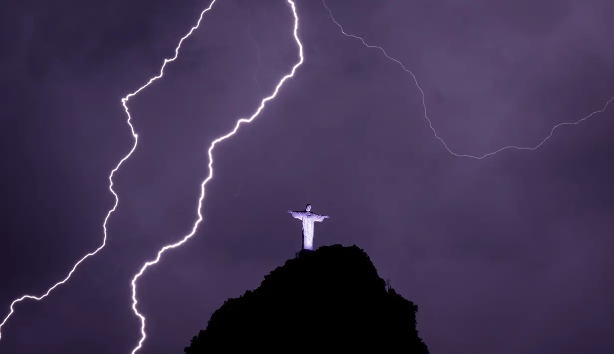 Petir menyambar di dekat patung Kristus Penebus di gunung Corcovado di Rio de Janeiro, Brasil, Selasa (21/2/2023). Pada 2007, Patung Yesus Kristus ini masuk dalam tujuh keajaiban dunia.  (Photo by MAURO PIMENTEL / AFP)