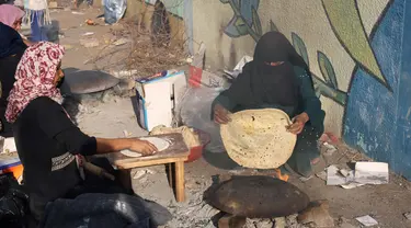 Para wanita Palestina membuat roti tidak beragi tradisional di atas api terbuka di salah satu lokasi penampungan pengungsi pada 27 Oktober 2023. (SAID KHATIB/AFP)