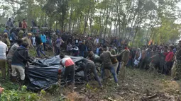 Polisi dan pekerja kehutanan bersama penduduk desa menutupi tubuh gajah betina dengan  plastik, yang sedang hamil, setelah kereta penumpang yang melaju menabrak dua gajah yang melintasi rel di desa Batasi dekat perbatasan India-Nepal, sekitar 37 km dari Siliguri (11/12/2019). (AFP/Diptendu Dutta)