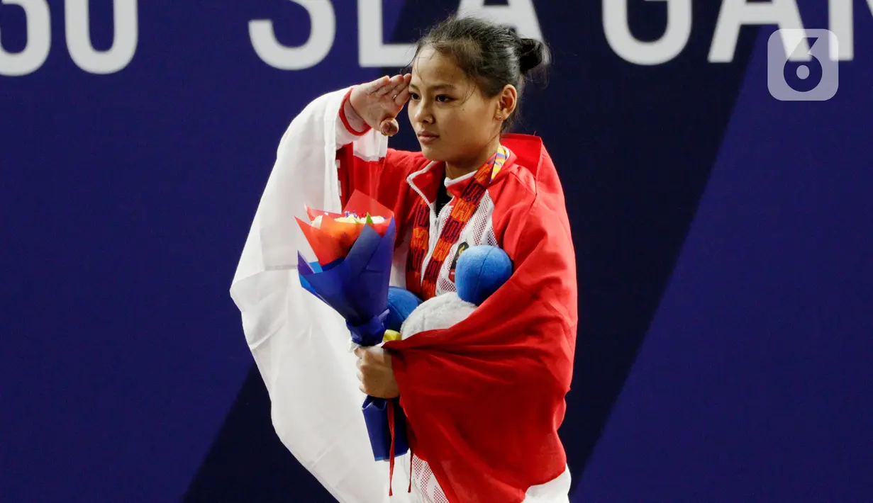 Lifter Windy Aisyah sikap hormat saat naik podium usai mendapatkan medali emas SEA Games 2019 cabang angkat besi nomor 49 kg di Stadion Rizal Memorial, Manila, Minggu (1/12/2019). Windy Aisyah meraih emas dengan total angkatan 104 kg. (Bola.com/M Iqbal Ichsan)