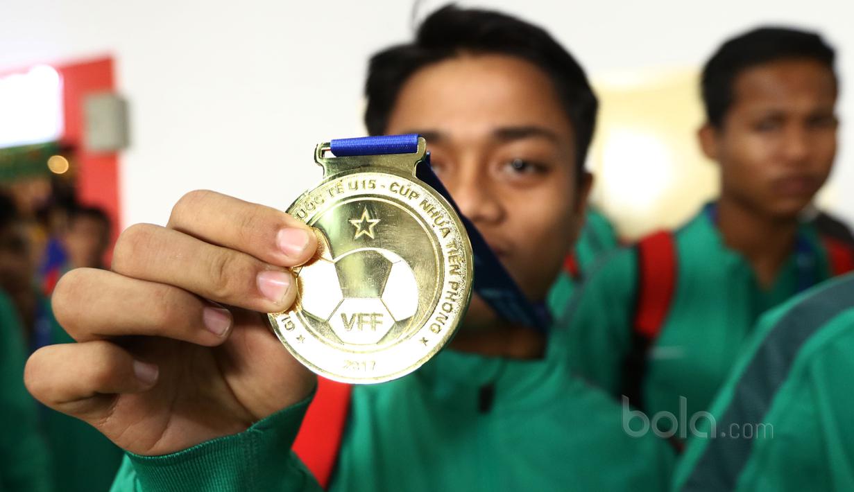 Seorang pemain Timnas Indonesia U-16 menunjukan medali emas yang diraih saat tiba di Bandara Soekarno-Hatta, Cengkareng, Senin (19/6/2017). Timnas U-16 menjadi juara pada ajang Tien Phong Plastic Tournament 2017. (Bola.com/Nicklas Hanoatubun)