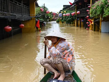Seorang perempuan mendayung perahu di jalanan yang terendam banjir setelah hujan deras di Hoi An, Vietnam, Kamis 30 Oktober 2025. Hujan deras dengan intensitas tertinggi sepanjang sejarah memicu banjir besar di Vietnam bagian tengah. (NHAC NGUYEN/AFP)