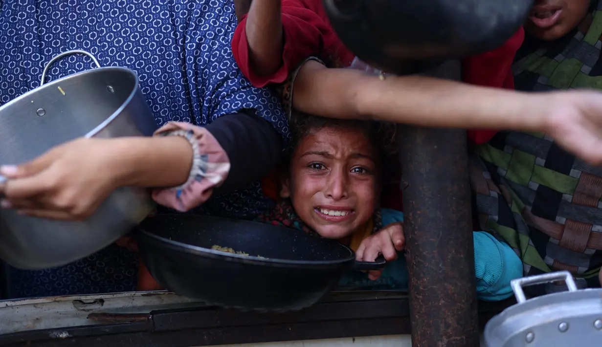 Seorang anak perempuan Palestina menunggu dalam antrean untuk menerima makanan di luar pusat distribusi di selatan Khan Yunis pada 6 Desember 2024. (BASHAR TALEB/AFP)