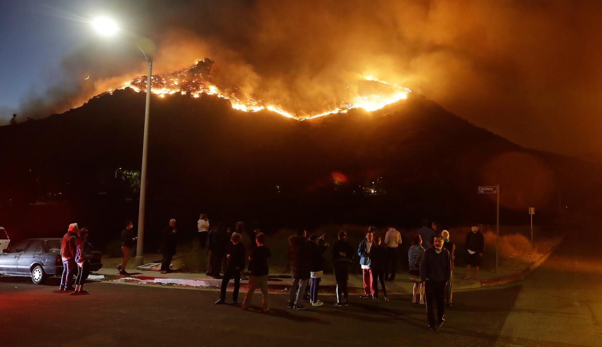 Warga menyaksikan kebakaran hutan dari sudut jalan di West Hills, California, AS, Jumat (9/11). Kebakaran ini dilaporkan telah menewaskan sembilan orang. (AP Photo/Marcio Jose Sanchez)