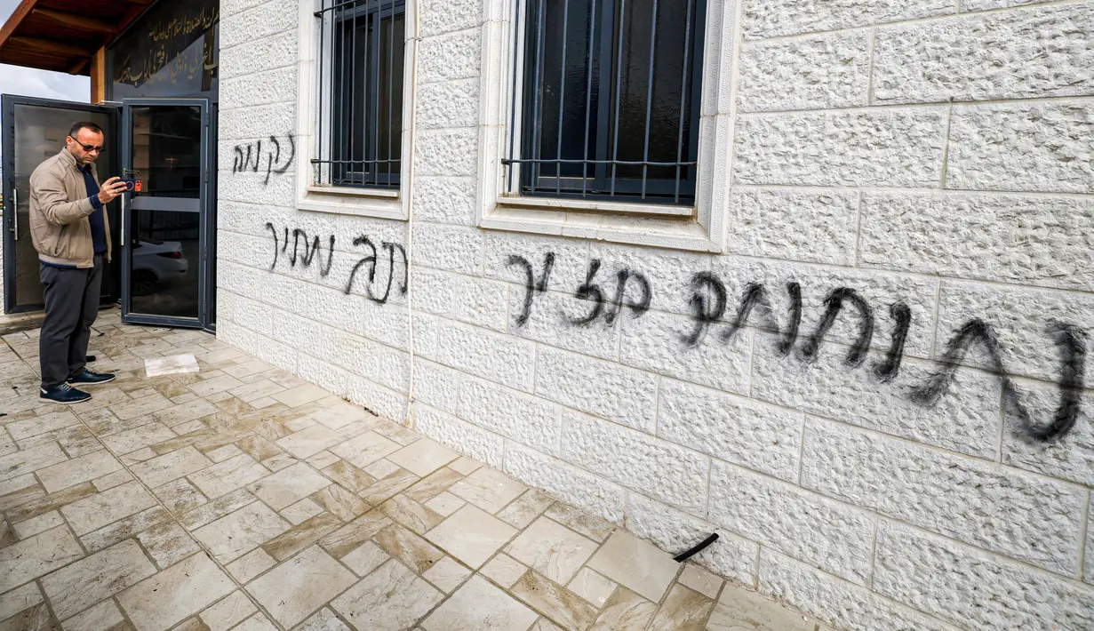 Para pemukim ilegal Israel juga mencoret dinding Masjid Abu Bakr as-Siddiq yang berada di antara Sarra dan Tal, dekat Nablus, wilayah utara Tepi Barat, dengan slogan-slogan rasis. Tampak dalam foto, seorang pria merekam coretan grafiti Ibrani pada dinding luar Masjid Abu Bakr al-Siddiq di desa Tell, sebelah barat Nablus, Tepi Barat yang diduduki, pada 23 Februari 2026. (JAAFAR ASHTIYEH/AFP)