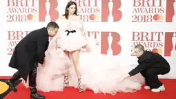 Dua orang pria membantu penyanyi cantik Dua Lipa merapikan gaunnya sebelum berpose di karpet merah acara Brit Awards 2018 di O2 Arena, London, Rabu (21/2). Ini adalah gelaran ke-38 untuk ajang penghargaan terbesar di Britania Raya. (Tolga AKMEN / AFP)