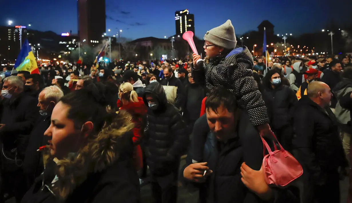 Seorang pria menggendong anak di pundaknya saat orang-orang yang memprotes pembatasan terkait pandemi COVID-19 berbaris di pusat Kota Bucharest, Rumania, Senin (29/3/2021). Ribuan pengunjuk rasa antipembatasan turun ke jalan di beberapa kota Rumania. (AP Photo/Vadim Ghirda)