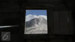 Gunung Sinabung terlihat dari puing jendela rumah yang rusak akibat luncuran awan panas pada April 2015 di Desa Sibintun, Karo, Sumatera Utara, Minggu (5/7). Akibat letusan Sinabung, desa tersebut sudah tak lagi berbentuk. (Liputan6.com/Johan Tallo)