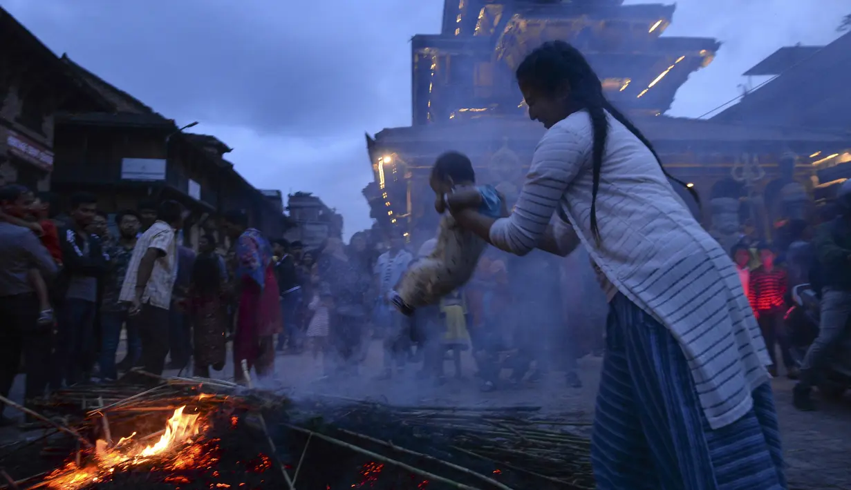 Seorang ibu mengasapi anaknya di sisa pembakaran patung iblis Ghantakarna selama Ghantakarna di kota kuno Bhaktapur, Nepal (30/7/2019). Menurut cerita setempat, setan Ghanta Karna suka menculik anak-anak dan perempuan. (AFP Photo/Prakash Mathema)