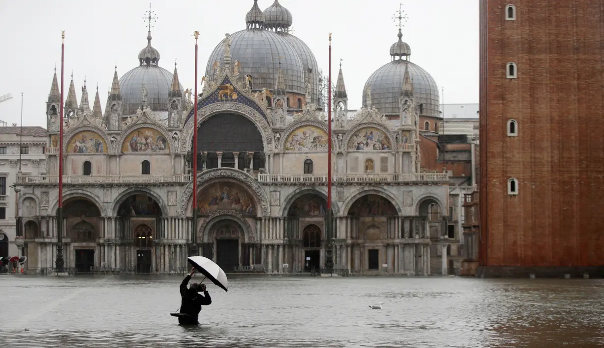 Fotografer mengambil gambar Alun-Alun Santo Markus yang banjir akibat gelombang pasang di Venesia, Italia, Selasa (12/11/2019). Venesia dilanda banjir akibat gelombang pasang setinggi 127 cm. (AP Photo/Luca Bruno)