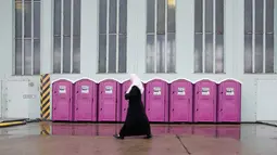 Seorang wanita berjalan melewati deretan toilet portable di tempat penampungan bagi para migran di dalam hanggar bekas bandara Tempelhof di Berlin, Jerman, Rabu (9/12/2015). (REUTERS/Fabrizio Bensch)
