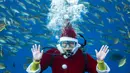 Seorang penyelam berpakaian seperti Sinterklas berpose di depan media saat dia memberi makan ikan dalam akuarium di Yokohama Hakkeijima Sea Paradise, Yokohama, Jepang, 10 Desember 2021. Walau populasi umat Kristiani hanya 1 persen, perayaan Natal di Jepang tetap meriah. (Philip FONG/AFP)